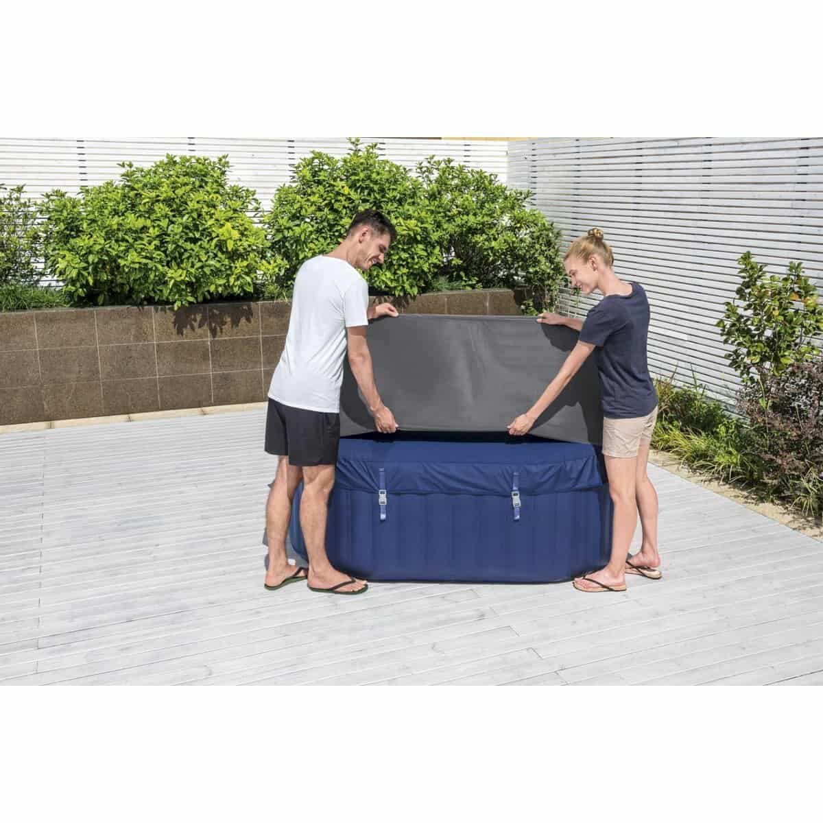 Twee mensen zetten een opblaasbaar zwembad op een terras met planten en houten vloer.