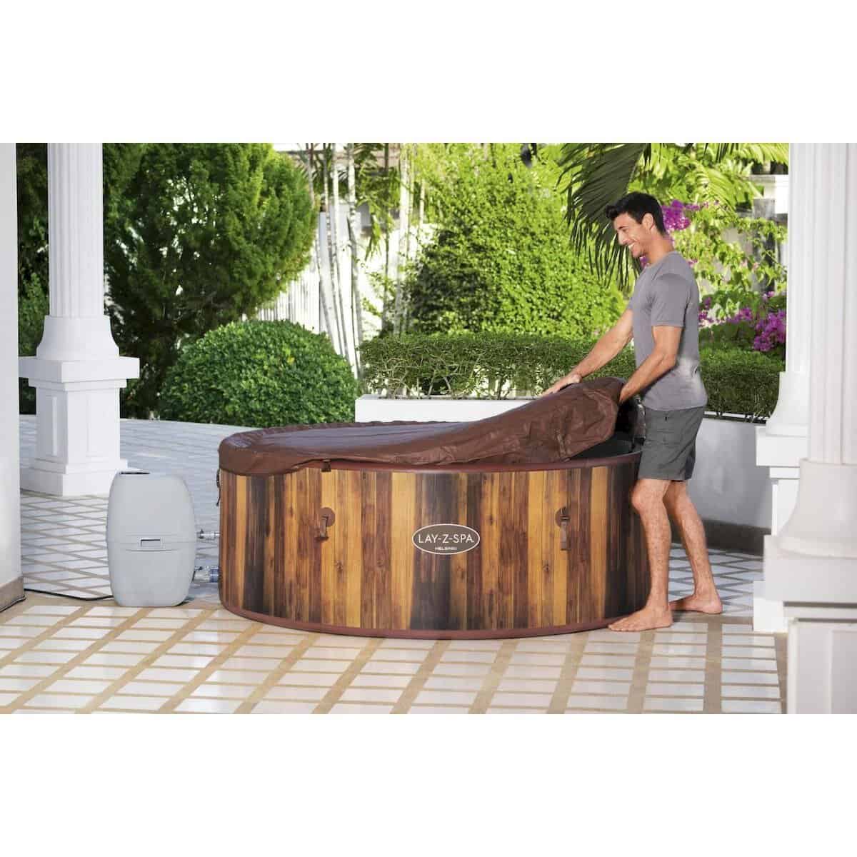 Luxe houten hot tub buiten in tuin met man die de cover verwijdert.