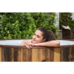 Ontspannen vrouw in een houten hottub, omgeven door groene tuin, perfect voor zomerplezier en wellne.